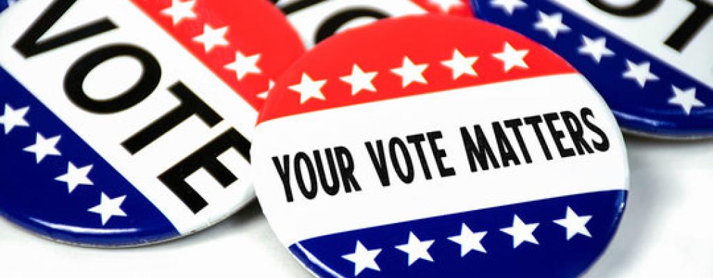 A pile of red white and blue buttons on a white surface. Text on the buttons reads "VOTE" and "YOUR VOTE MATTERS."