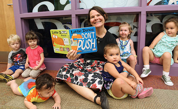 Youth Services Librarian holding a book surrounded by toddlers