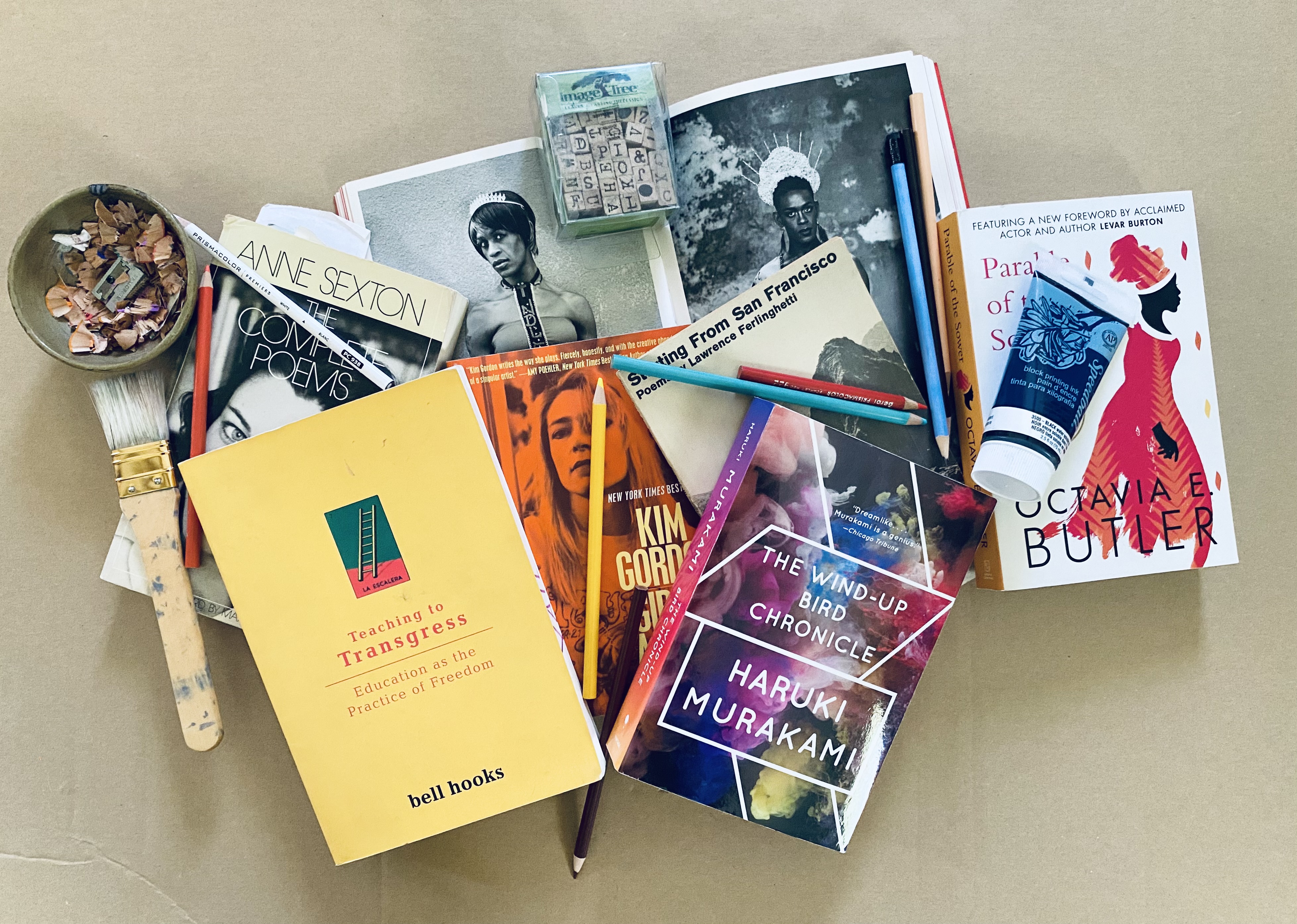 Variety of eight books scattered across a desk with paint, pencils, paint brush and pencil shavings scattered among them 