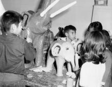 Children stand around a table painting paper-mache elephants