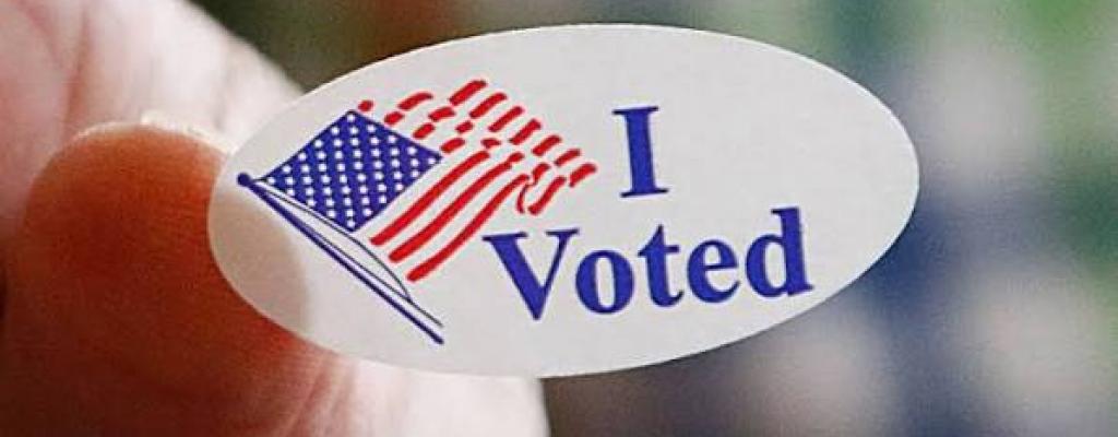 Hand holding an "I Voted" sticker from a polling location 