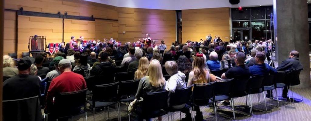 a large seated audience faces a brass band at the front of room