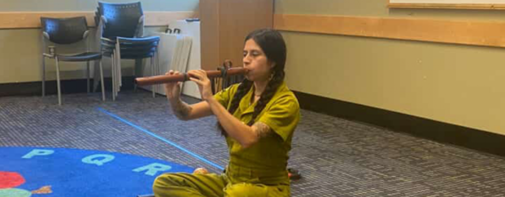 Chiara Beaumont sitting cross legged playing a wind instrument