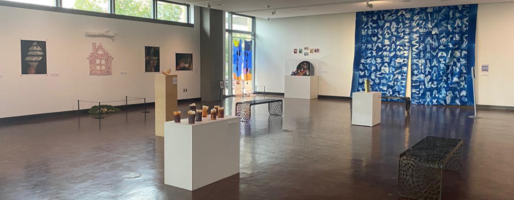 Library gallery view of art hanging on walls, sculptures along the wall, and in acrylic display cases