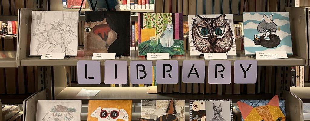 Five book shelves with 4 inch by 4 inch paintings and collaged art of community member's pets. The words Menchaca Road Library community exhibit run across the bottom of the book shelves