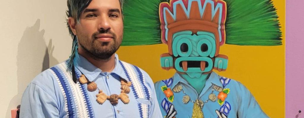 artist Luis Coss standing in front of a brightly colored, Mayan inspired figurative painting