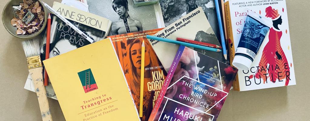 Variety of eight books scattered across a desk with paint, pencils, paint brush and pencil shavings scattered among them 