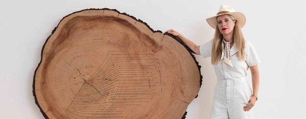 woman standing next to a cross section of a tree that's on a stand. Timeline of moments across women's history are etched into the tree ring