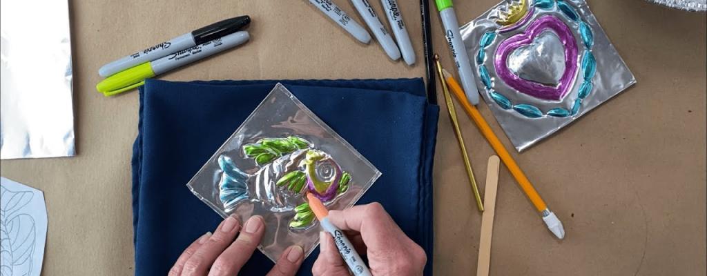 Hands coloring their fish design tin art with Sharpie colored markers.