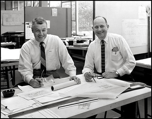 Charles Granger and Arthur Fehr sitting at a table covered in drawings.